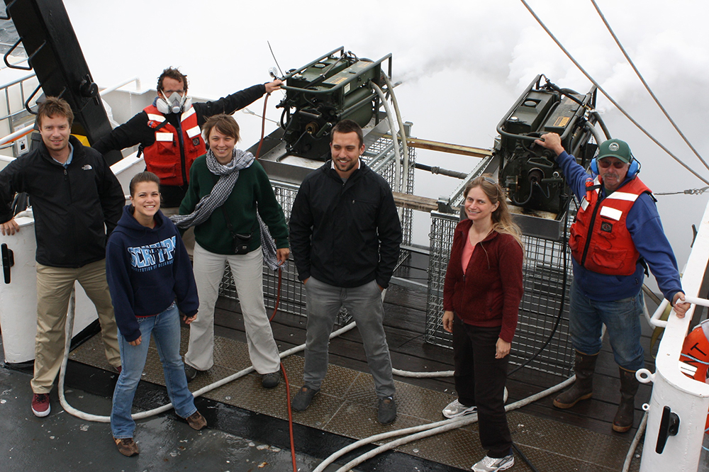Seven researchers stand together on a ship deck for a photo at sea.