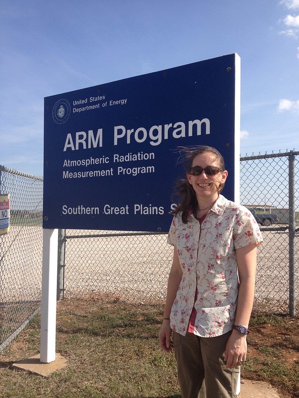 Sally McFarlane stands in front of a sign that says, "ARM Program, Atmospheric Radiation Measurement Program, Southern Great Plains."