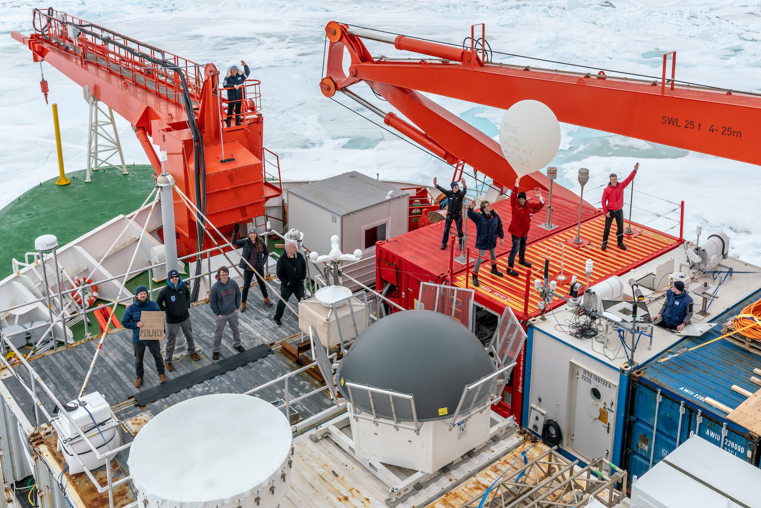 MOSAiC Atmosphere team members stand amid instruments and containers to wave from the bow of the Polarstern