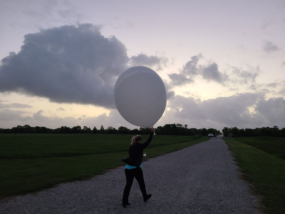 Michelle Kiani walks down a path while holding a weather balloon overhead.