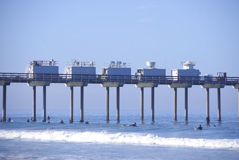 ARM instruments and containers line the middle of Scripps Pier as beachgoers frolic in the waves below.