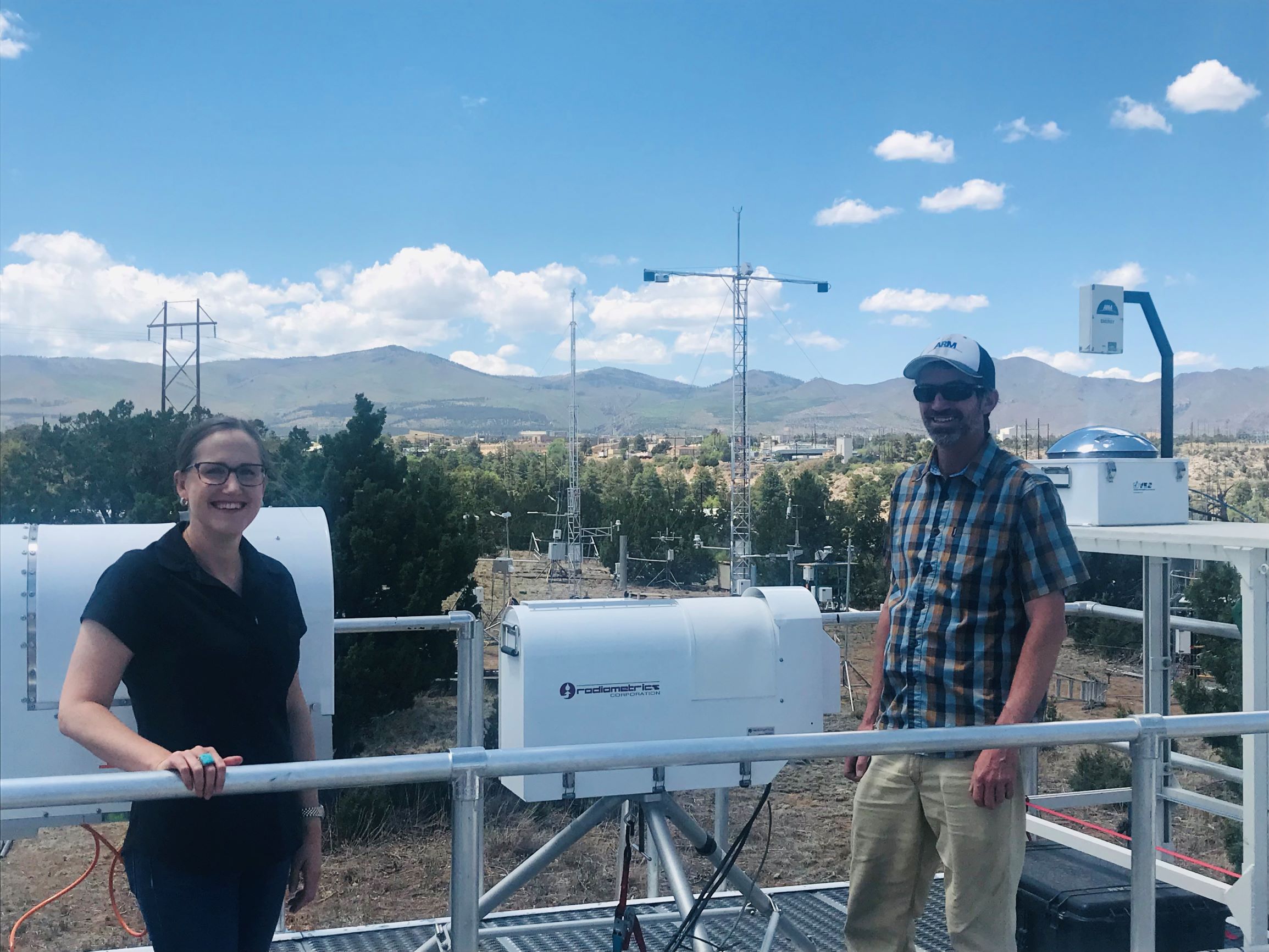 Allison Aiken and John Bilberry poses with microwave radiometers and a total sky imager at Los Alamos National Laboratory.
