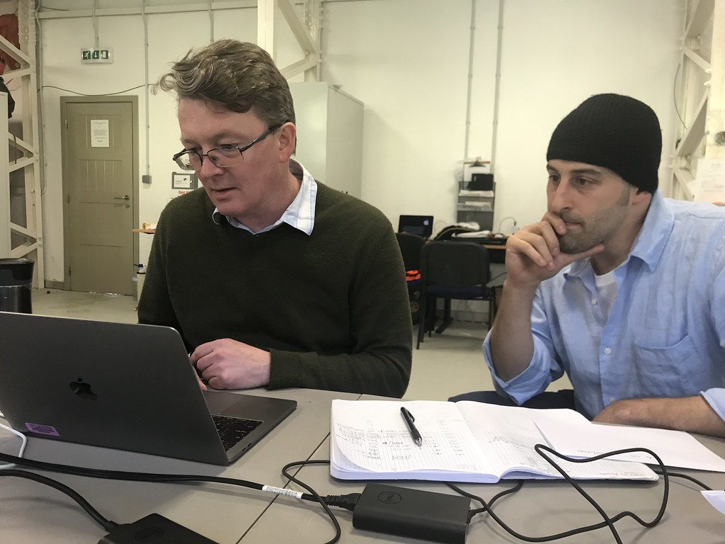 Rob Wood and Scott Giangrande look at a computer screen together. A pen and notebook are on the table in front of Giangrande.