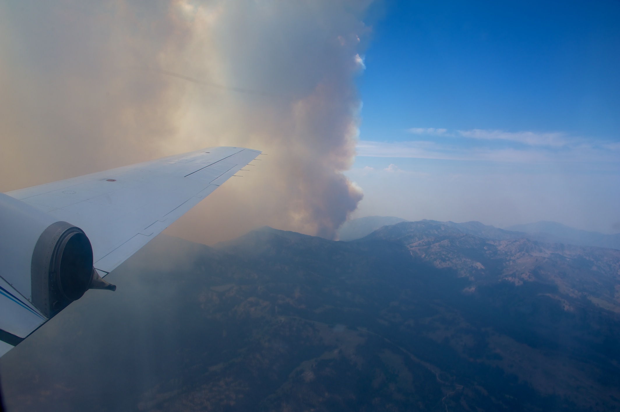 The wing of the Gulfstream-159 research aircraft extends into the camera frame. Just beyond the wing is a plume of wildfire smoke.