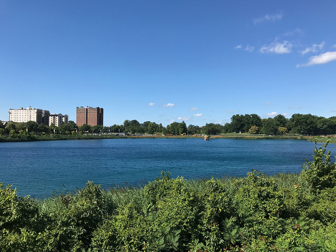 A blue Druid Lake on a mostly clear day, with buildings on the other side of the lake