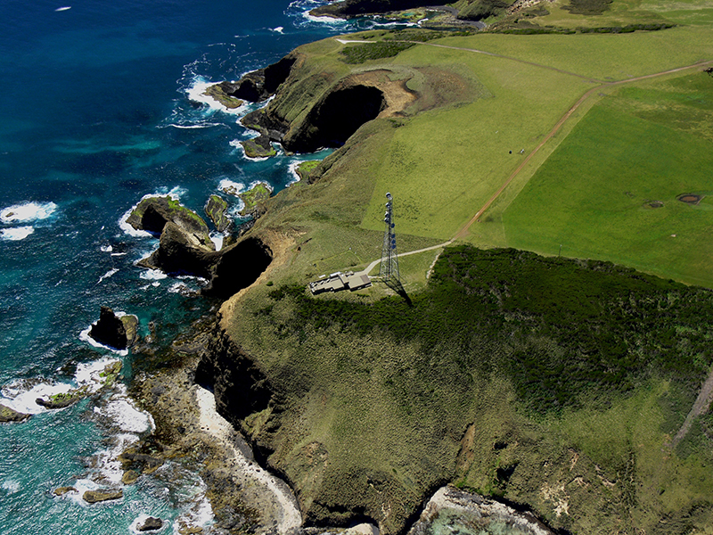 An aerial photo looks down on the Kennaook/Cape Grim Baseline Air Pollution Station, which is bordered by water below.