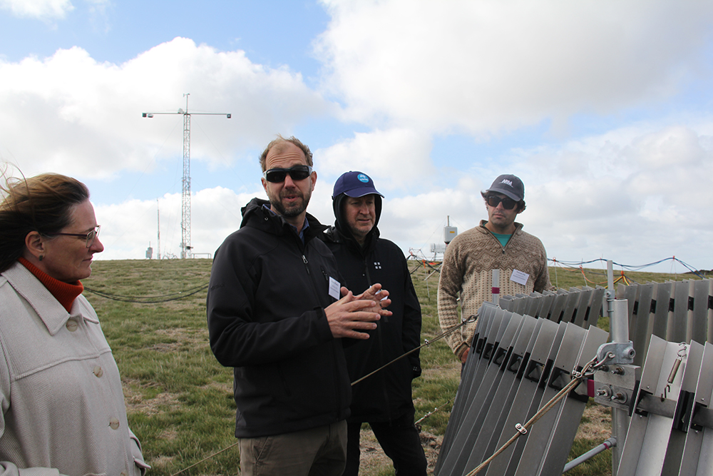 ARM Mobile Facility Site Manager Heath Powers gestures while standing in front of an ARM rain gauge at the CAPE-k site in April 2024. Photo is by Sophie Schmidt, CSIRO.
