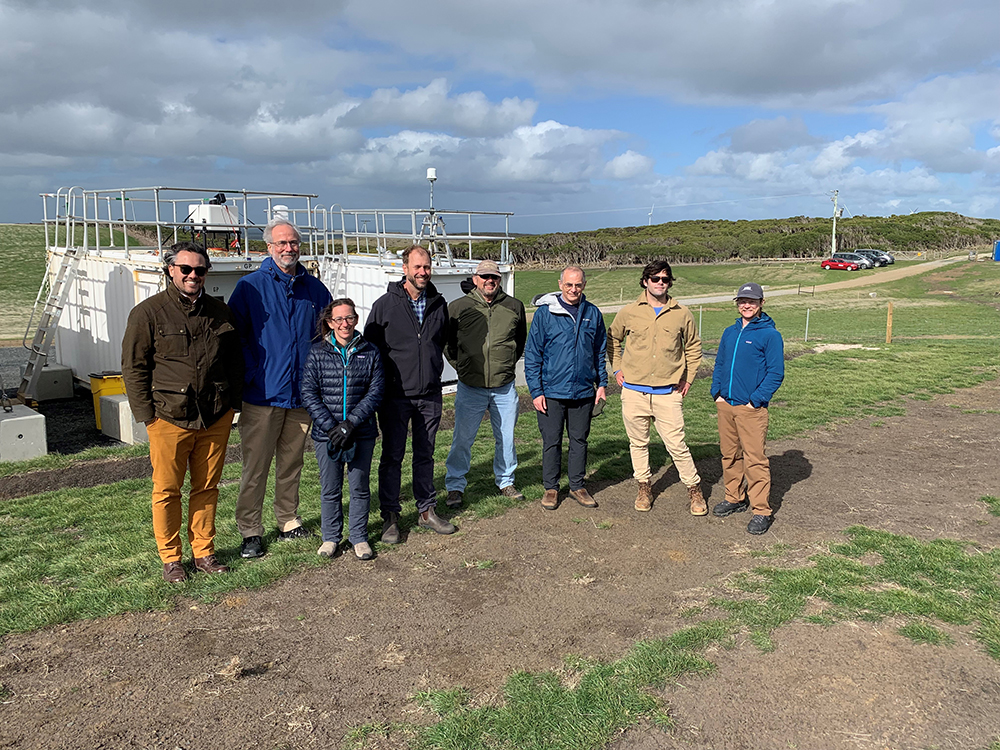With clouds overhead, a group of CAPE-k visitors and site staff take a photo in front of the ARM Mobile Facility at kennaook / Cape Grim, Tasmania. Pictured from left to right are Josh Shiode, DOE Office of Science senior advisor; Patrick Fitch, an associate laboratory director at Los Alamos National Laboratory; Sally McFarlane, DOE ARM program manager; Heath Powers, who manages the ARM Mobile Facility deployed for CAPE-k; Jay Mace, CAPE-k’s co-principal investigator from the University of Utah; Jim Mather, ARM director; and Tom Day and Frank Zurek, both CAPE-k site technicians. Photo is courtesy of McFarlane.