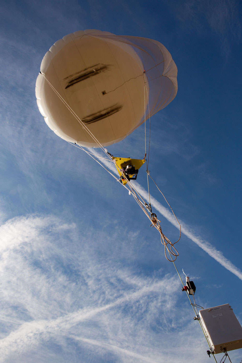 A tethered balloon is aloft in the sky with instruments installed on the tether.