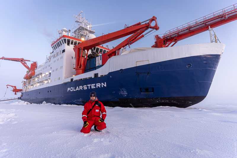 Janek Uin kneels in front of the Polarstern during the MOSAiC expedition