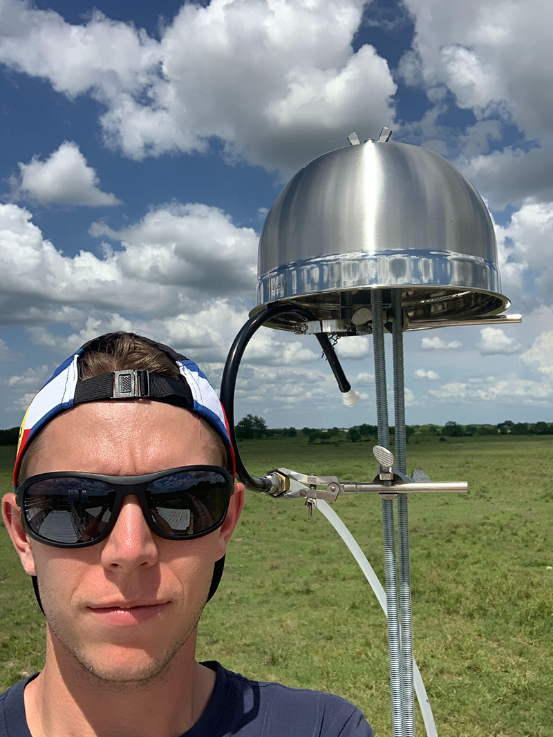 Carson Hume stands next to an instrument with a salad bowl turned upside down on top to protect the ice-nucleating particle filters from precipitation.