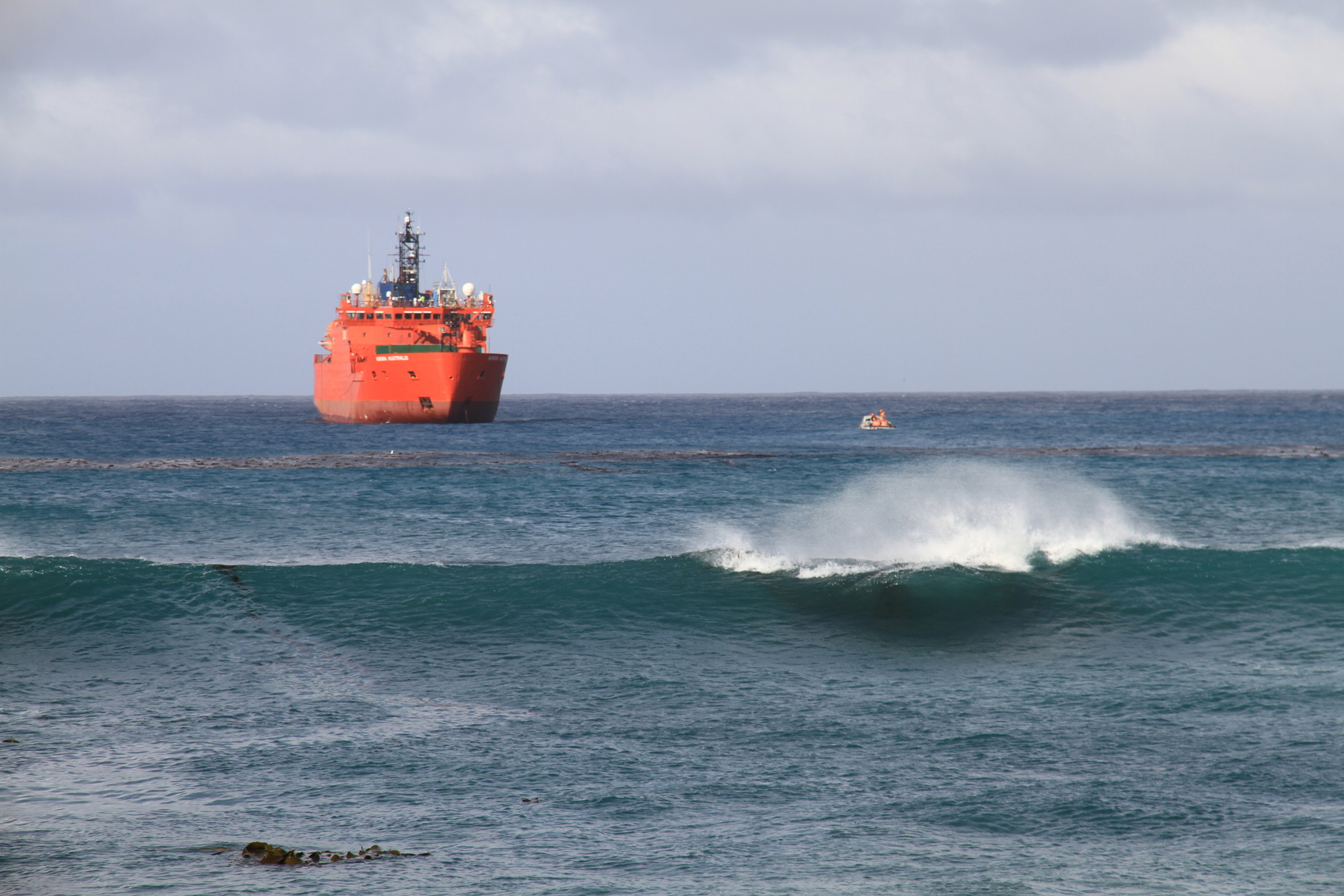 Orange supply vessel travels across the ocean with waves forming in front