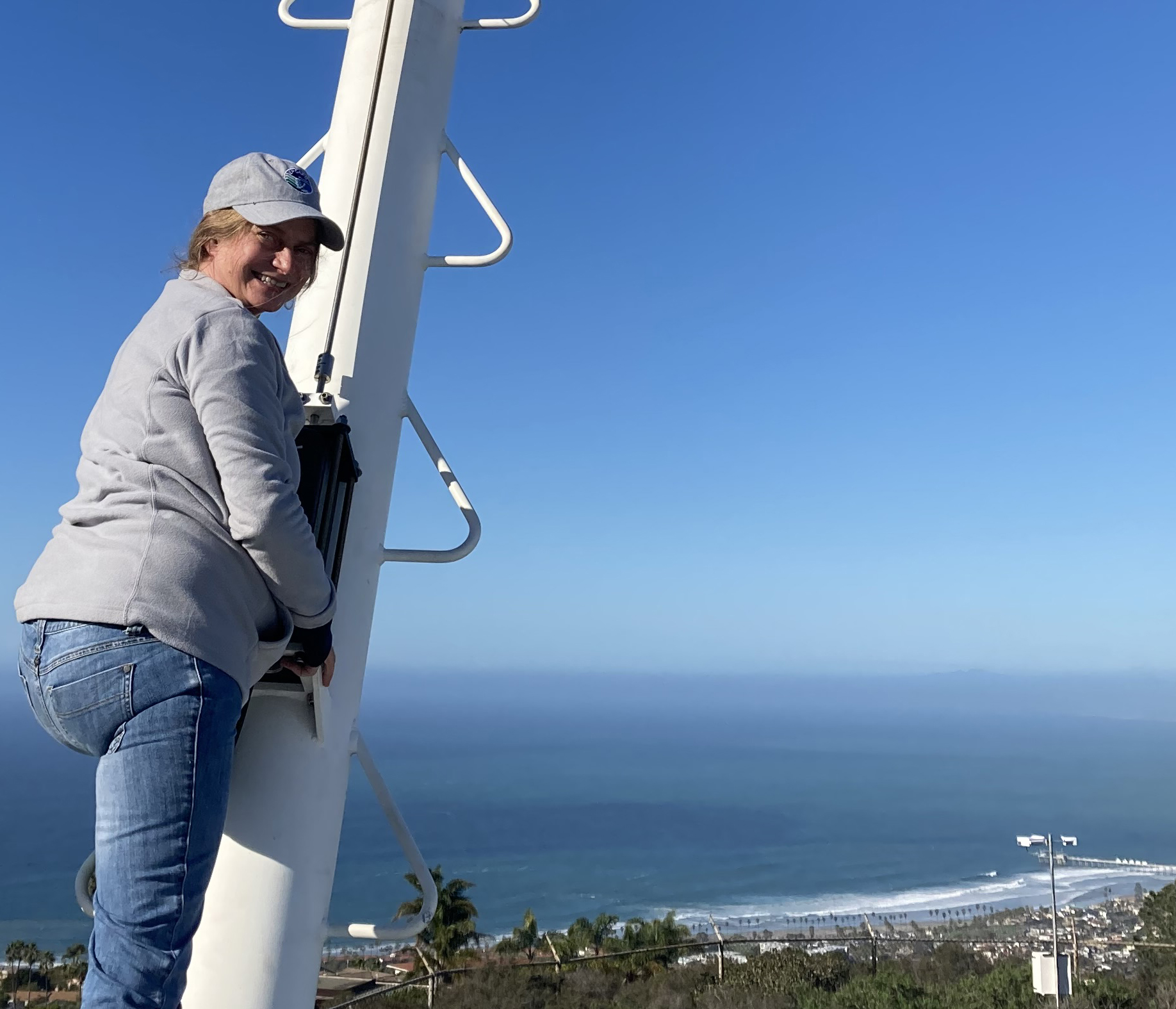 On a clear day in La Jolla, California, Lynn Russell stands on her aerosol sampling van overlooking trees, buildings, and the Pacific Ocean below.