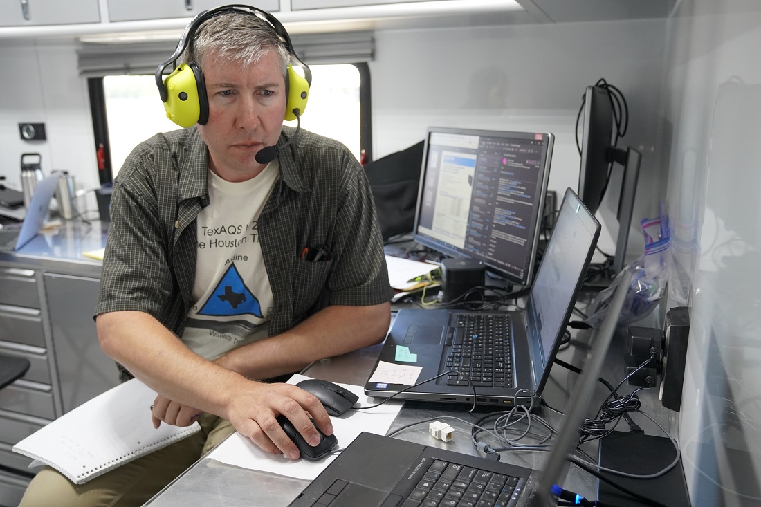 Wearing headphones, Matt Newburn reviews flight data on a computer inside a ground control station.