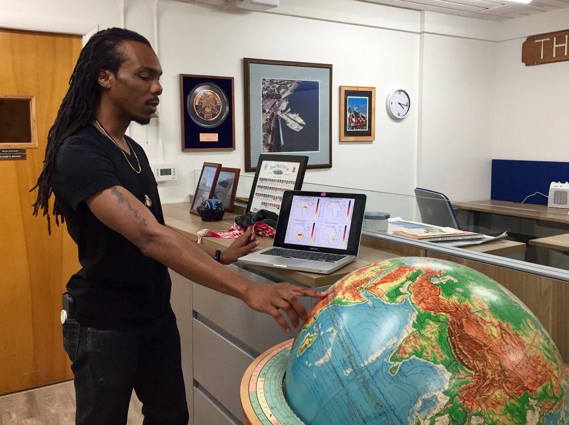 Osinachi Ajoku points to Africa on a globe while standing next to an open laptop.