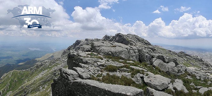 Mountainous terrain with a view of fields below and clouds floating across the horizon