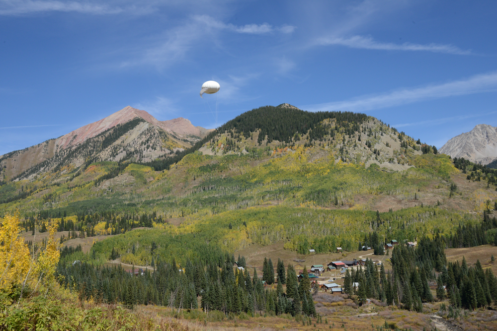 A white tethered balloon hovers over the Gothic, Colorado, site with Gothic Mountain in the background. 