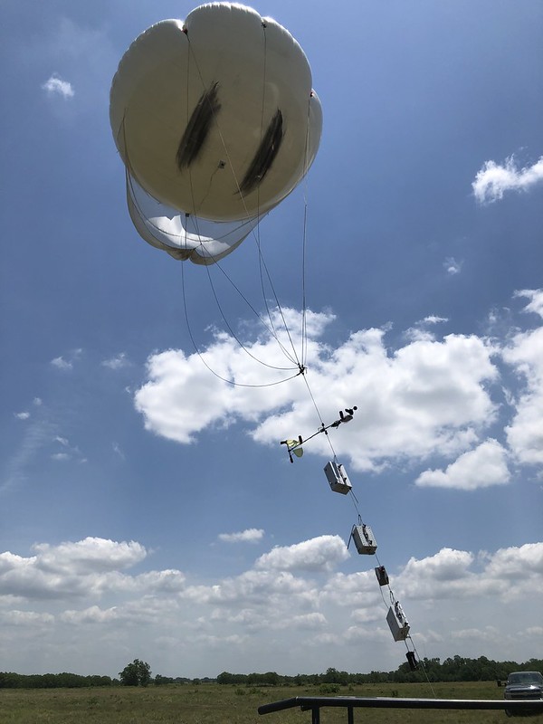 Puffy clouds serve as a backdrop for instruments strung to a tethered balloon.