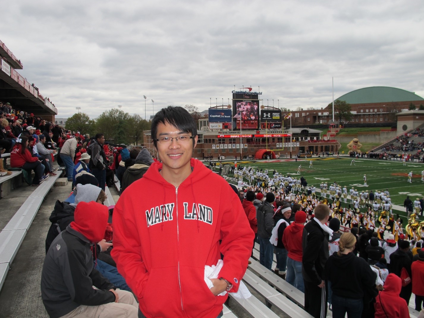 Youtong Zheng smiles for the camera wearing a Maryland sweatshirt at a football game.