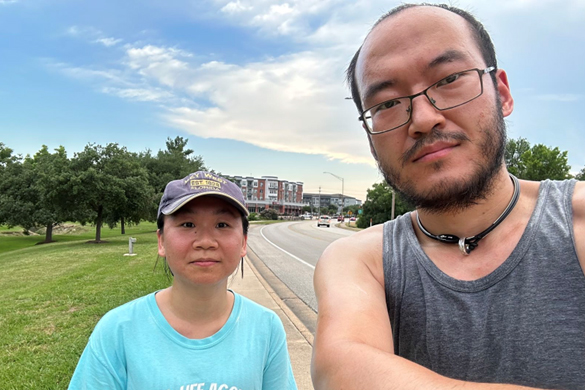 Yunpeng Shan takes a photo of himself and his wife, Lin Lin, on a sidewalk lining a city greenspace.