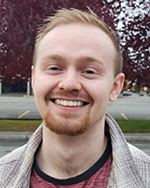 Hunter Barndt poses for a photo outside in front with a tree with dark burgundy leaves.